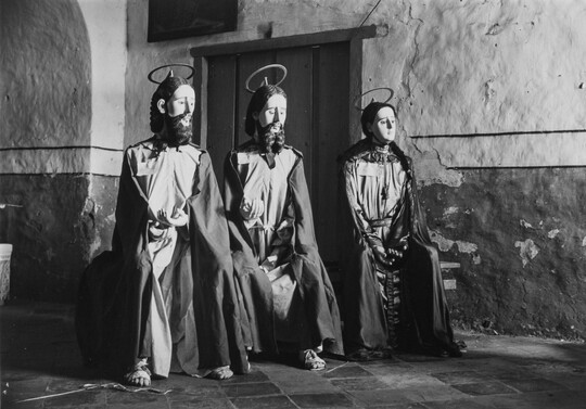 A black-and-white photograph of three seated mannequins, two with beards, wearing tunics and loose robes, sandals, and with halos mounted on their heads.