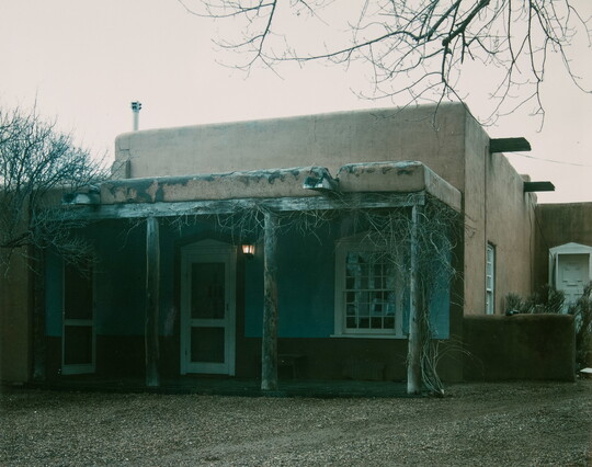 A color photograph of an adobe building with a wooden porch.