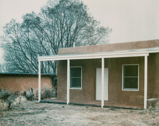 A color photograph of an adobe building with a wooden porch.