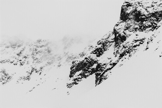 A black-and-white landscape photograph of a snowy mountain range.