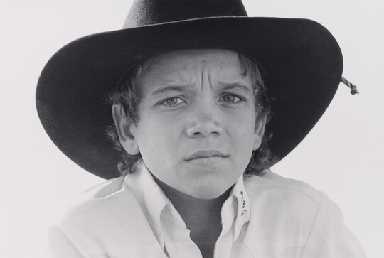 A black-and-white close-up portrait photograph of a White boy with a serious expression wearing a cowboy hat.