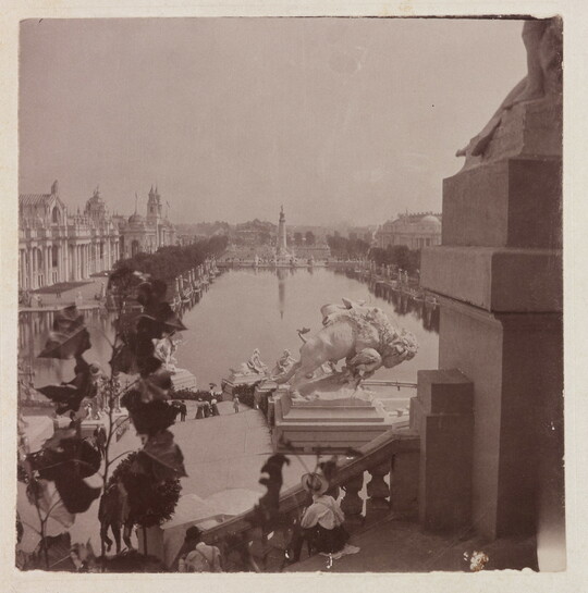 A black-and-white photograph of a tree-lined reflecting pool taken from the steps of a building showing other buildings and several sculptures, including a bison, lining the pool.