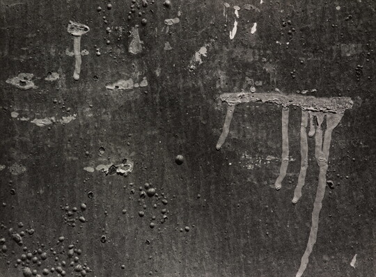 A black-and-white photograph of a close-up of paint drips on a wall.