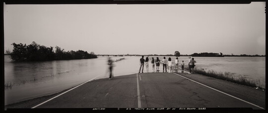 A black-and-white panoramic photograph of a group of people standing on a flooded street.