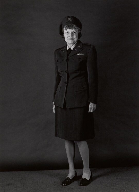 A black-and-white portrait photograph, in full length, of an older White woman wearing a military uniform that includes hat, jacket, and skirt.