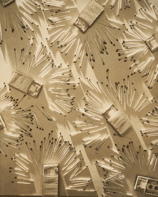 A sepia-toned photograph of wooden matches and opened matchboxes organized in a pattern on a light background.