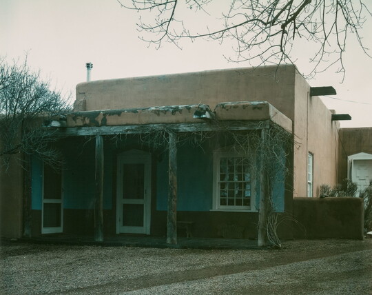 A color photograph of an adobe building with a wooden porch.
