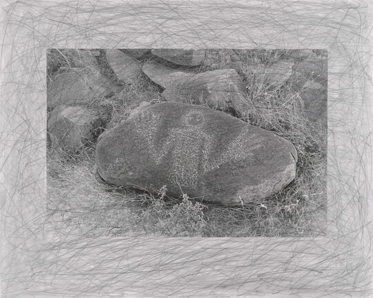 A black-and-white photograph of an oval-shaped stone with a human figure, hands held up, drawn in white on its surface.