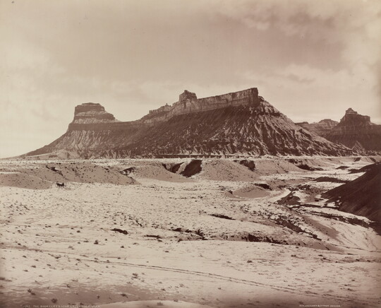 A sepia-toned photograph of a desert landscape with a rocky mesa in the distance.