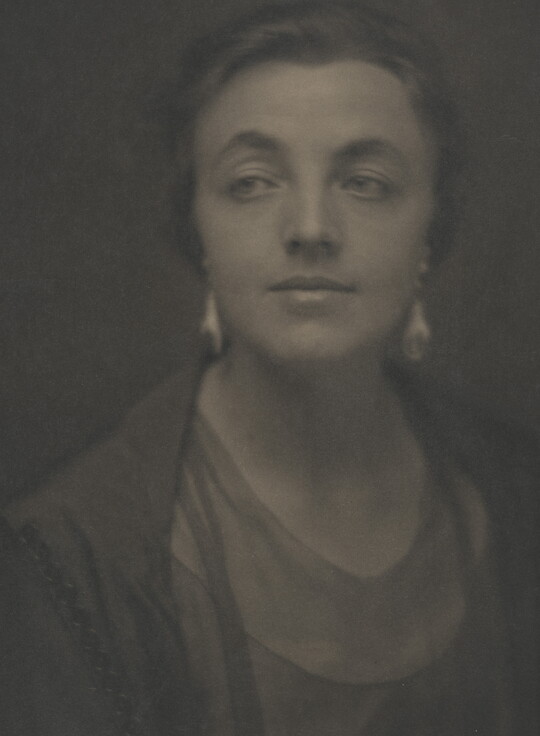 A sepia-toned portrait photograph of a White woman, hair tied back to show her dangling earrings.