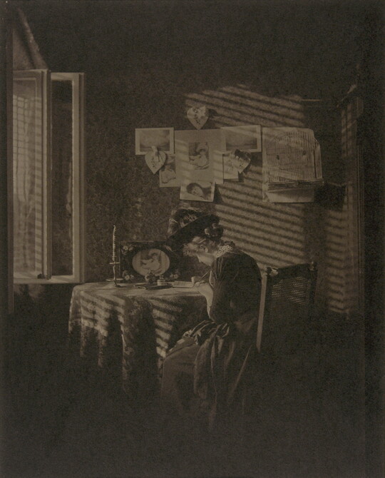 A sepia-toned photograph of a seated woman writing at a table, illuminated by light from a window.