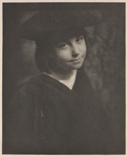 A black-and-white portrait photograph of a smiling, young White girl wearing a black hat and a black dress.