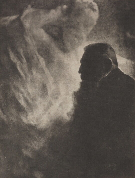 A soft-focus, black-and-white photograph of an older man with a big beard in profile against a light gray, almost smokey, background.