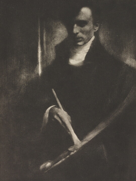 A dark, soft-focus black-and-white photograph of a White man looking down at a paintbrush and palette in his hands.