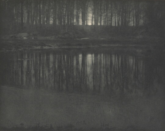 A black-and-white photograph of trees and moonlight reflected in calm water.