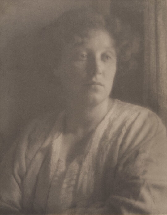 A black-and-white portrait photograph of a young White woman with curly hair wearing a white top.