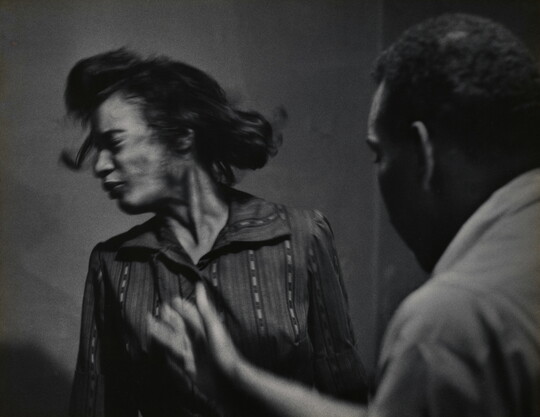A black-and-white, mid-action photograph of a Black man who has just slapped a Black woman whose face turns away in reaction.