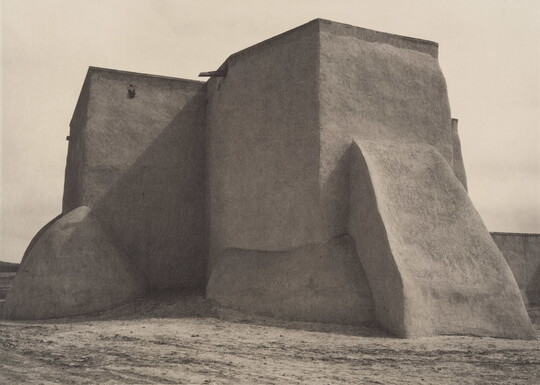 A black-and-white photograph of an adobe church from the back.