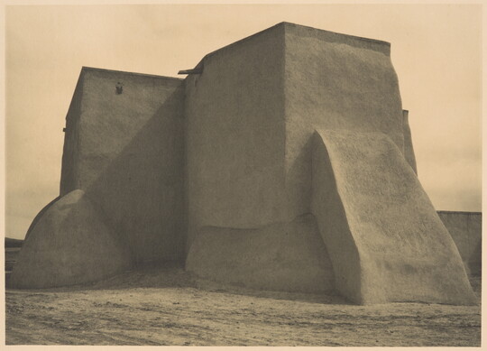 A black-and-white photograph of an adobe church from the back.