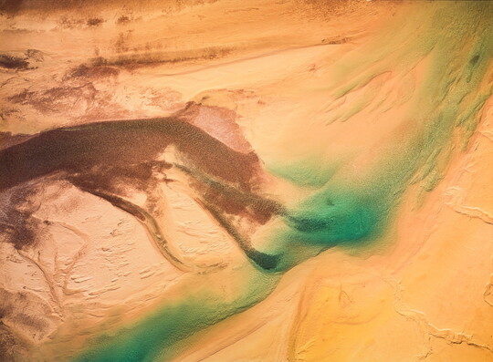 A color photograph of sand dunes from the air with a bright blue-green streak across them.