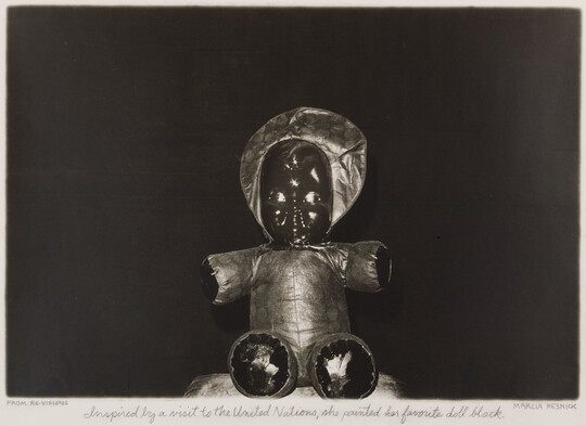 A black-and-white photograph of a seated doll with a soft body and a painted black face.