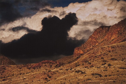 A color photograph of storm clouds gathering over a barren mountain landscape.