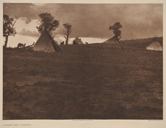 A sepia-toned photograph of a hilltop campsite with tipis amongst the scattered trees.