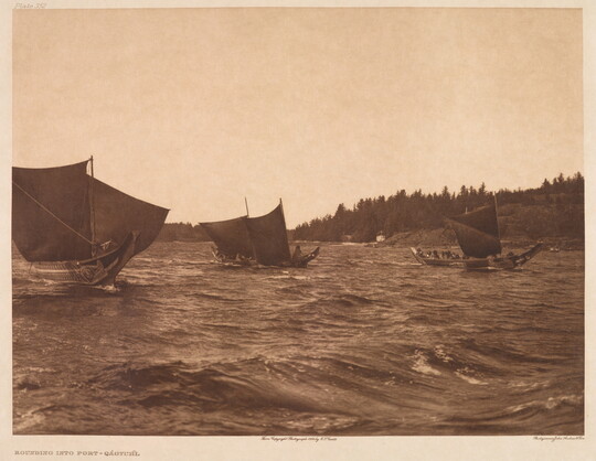 A sepia-toned photograph of three elaborately carved canoes with raised sails on choppy water.