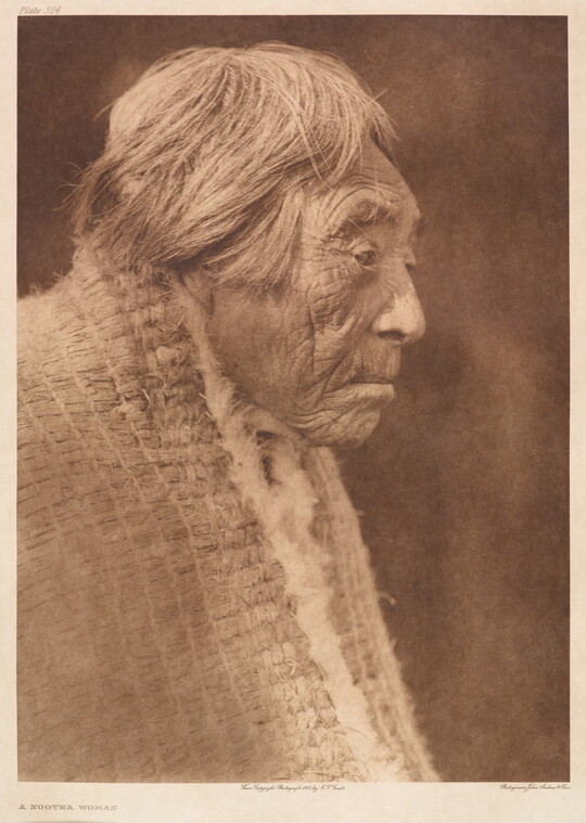 A sepia-toned portrait photograph of an elderly Indigenous woman, in profile, with short hair wearing a shawl around her shoulders.