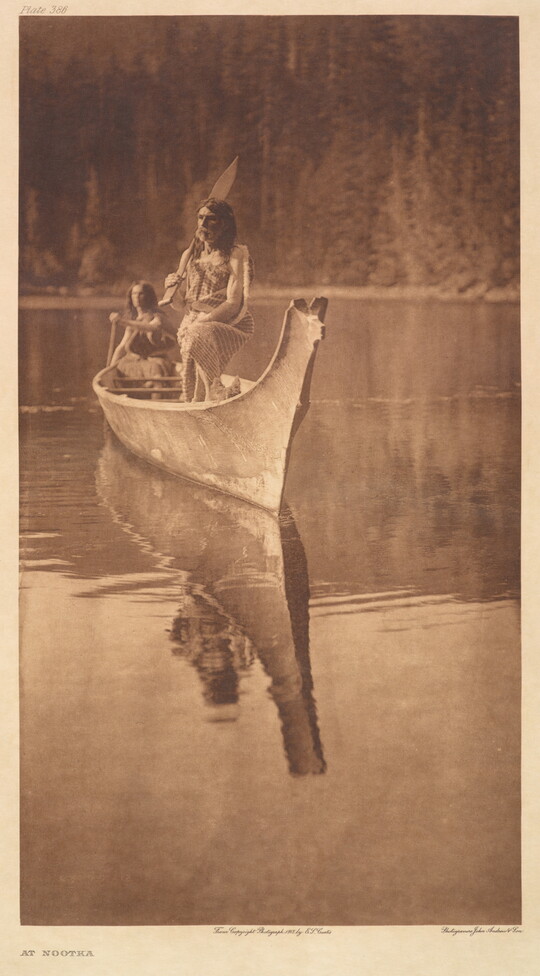 A sepia-toned photograph of two Indigenous people in a canoe floating on calm water.