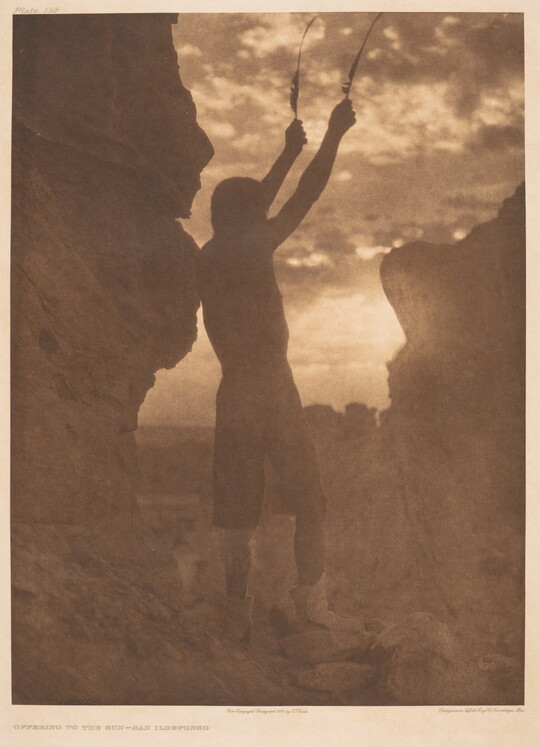 A sepia-toned photograph of a person in silhouette, arms raised in the air, standing between two large rocks.