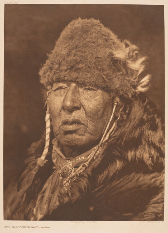 A sepia-toned portrait photograph of an older Indigenous person wearing fur clothing and a fur hat.