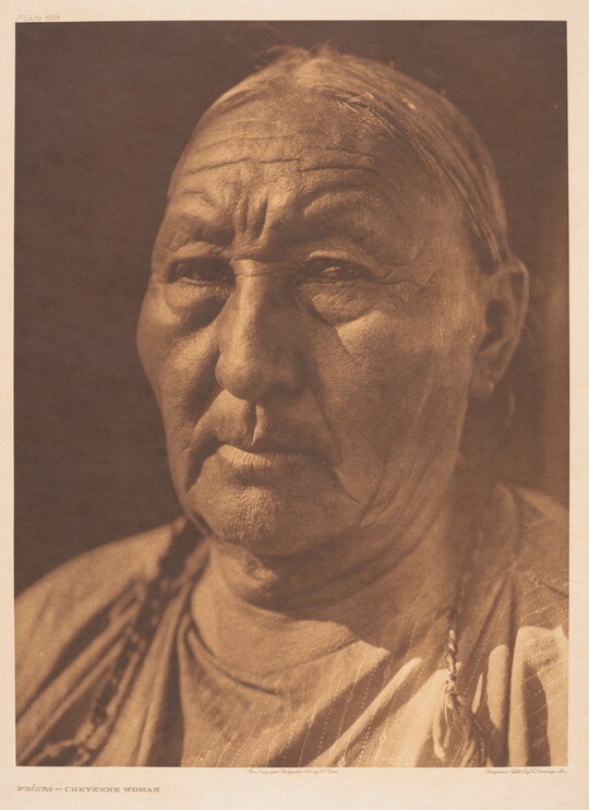 A sepia-toned portrait photograph of an older Indigenous woman with her hair in braids.