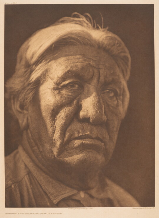 A sepia-toned portrait photograph of an older Indigenous man from the shoulders up wearing a collared shirt buttoned at the neck.