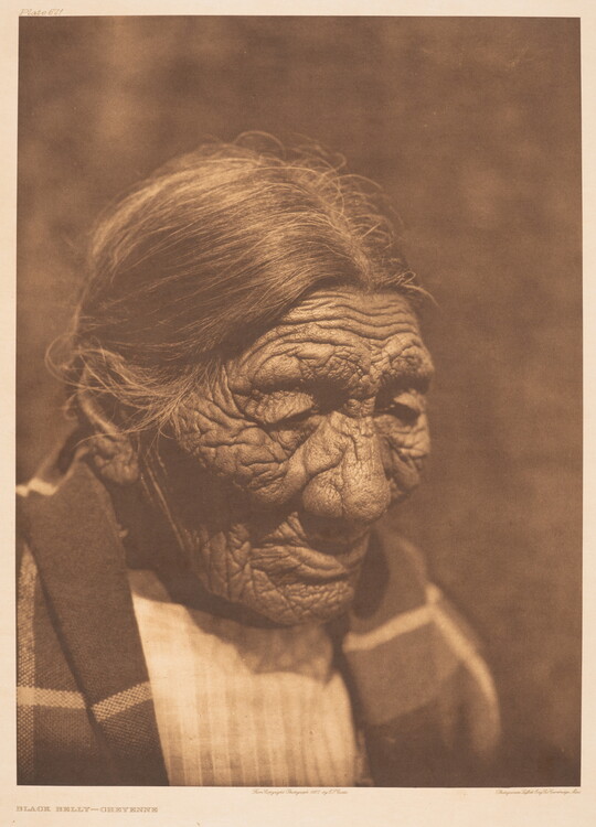 A sepia-toned photograph of an elderly Indigenous person with hair pulled back and a blanket around their shoulders.