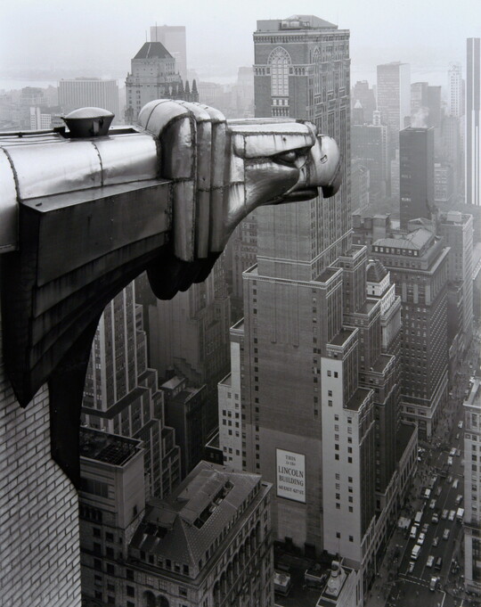 A black-and-white photograph of an Art-Deco gargoyle of an eagle overlooking the New York cityscape.