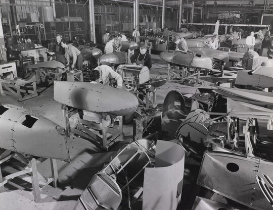 A black-and-white photograph of adult workers in an aircraft factory manufacturing aircraft parts.