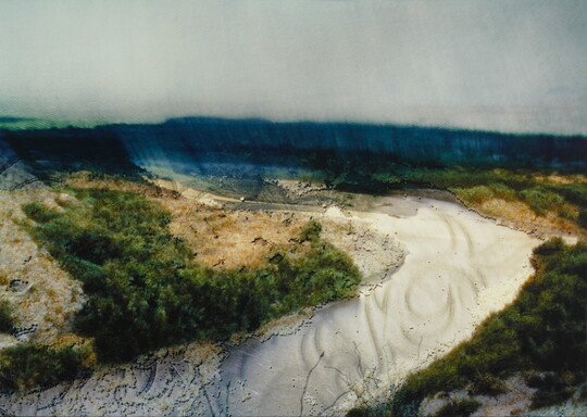 A slightly blurry color photograph of a river valley in vibrant blues, greens, and whites.
