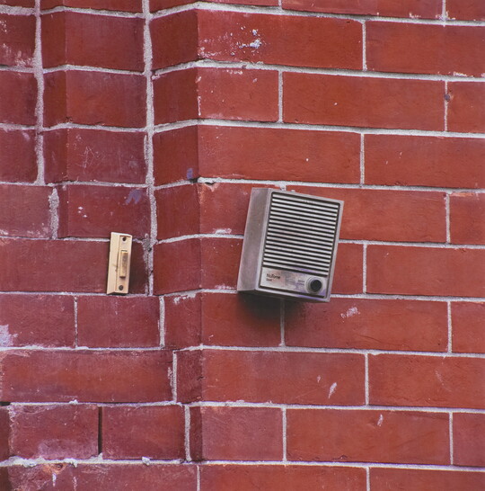 A color photograph of a doorbell and an intercom on a red brick wall.