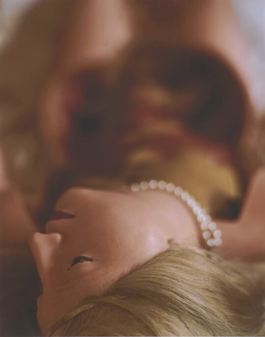 A color photograph of a White female wax mannequin with blonde hair and pearls laying down with head at the bottom of the image.