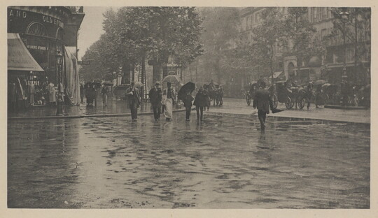 A black-and-white photograph of people crossing a city street in the rain.