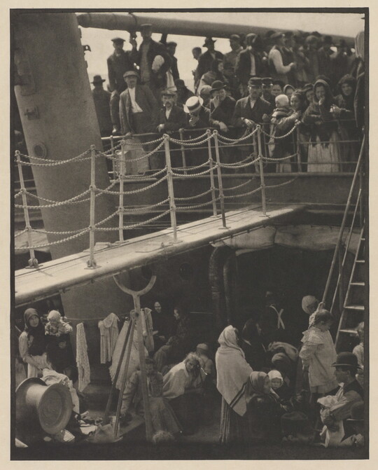 A black-and-white photograph of people outside on two decks of a crowded ship.