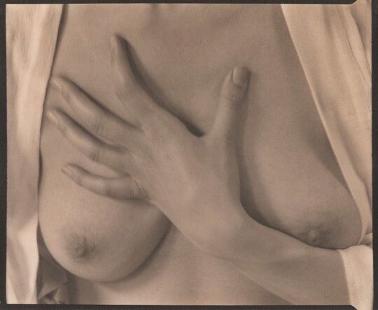 A sepia-toned photograph of the torso of a White woman with her hand on her bare chest between her breasts.