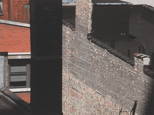 A color photograph of brick city building sides and rooftops as seen from another building window.