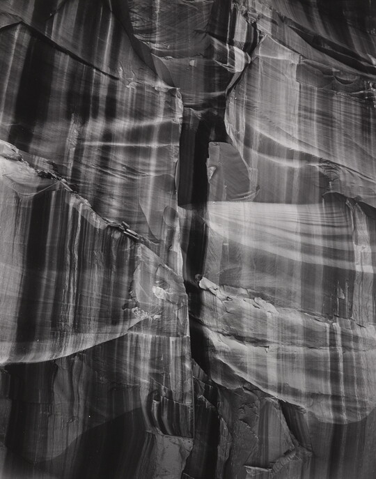 A black-and-white abstract photograph of a close up of a rocky canyon wall with vertical stripes.