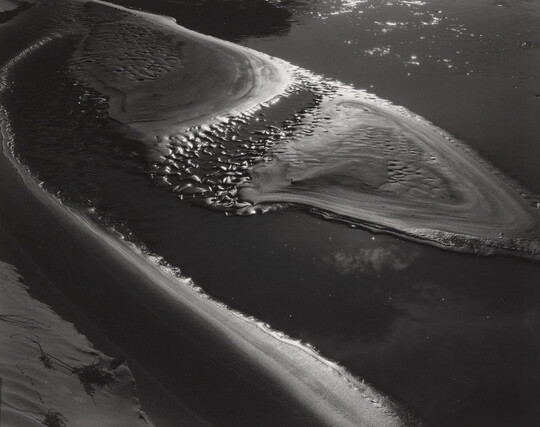 A black-and-white abstract photograph of water washing up on a sandy beach.