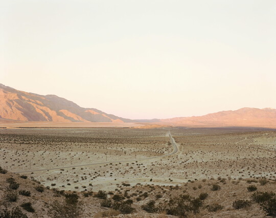 A color photograph of a desert landscape with sunlight reflecting off distant mountains.