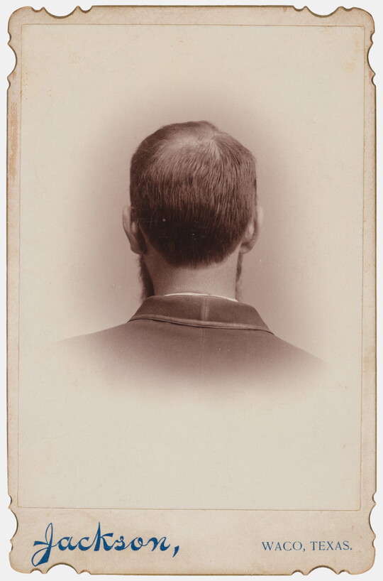 A black-and-white studio portrait photograph of the back of the head, from the neck up, of a man with short hair.