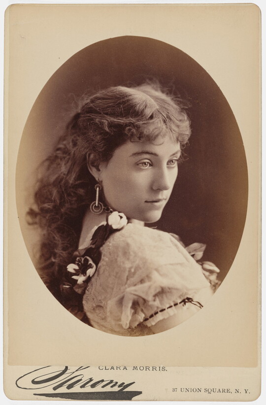 A sepia-toned studio portrait photograph, framed in an oval, of a young White woman gazing over her shoulder.
