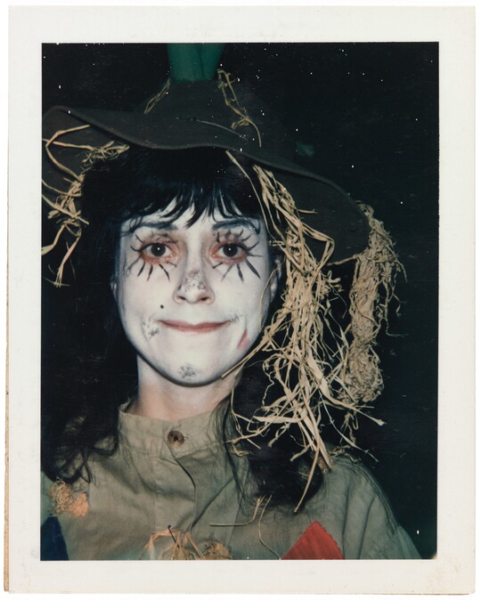 A color portrait of a girl wearing white face paint and dressed as a scarecrow.